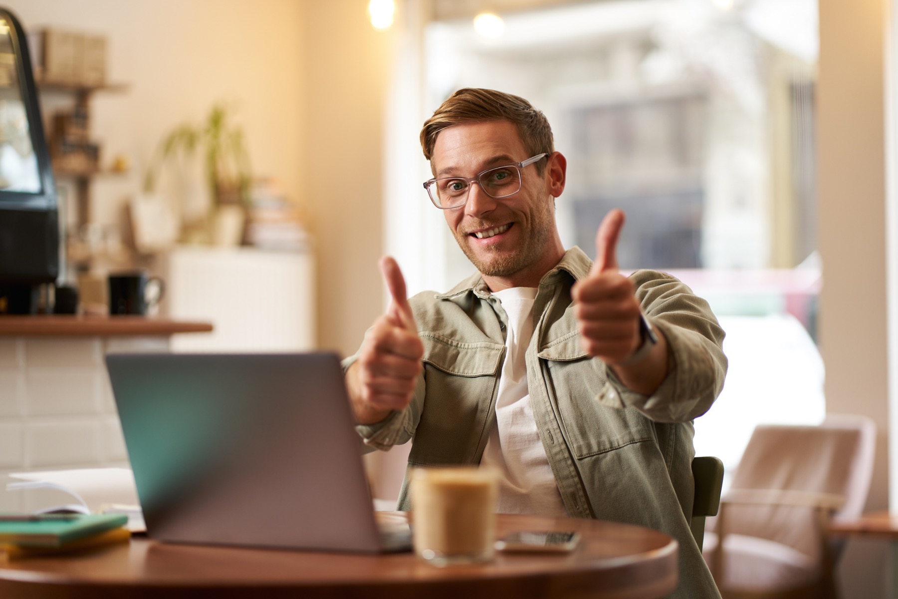 A smiling business owner working at a laptop and giving a thumbs-up