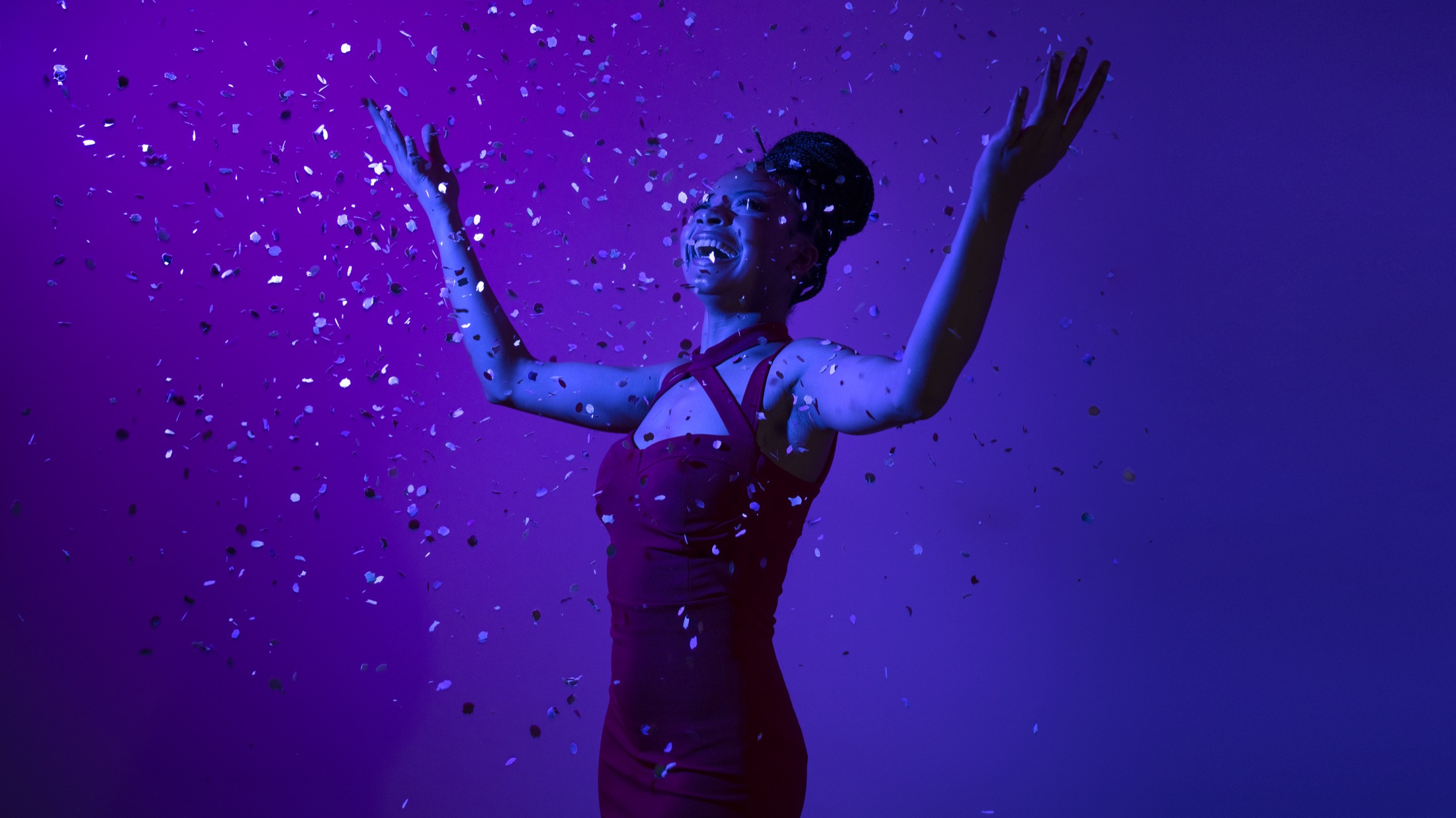 A woman celebrating under confetti in vivid purple light